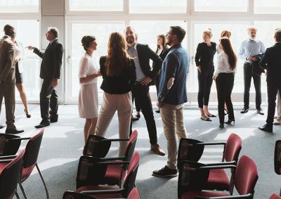 Group of people in fashionable office clothes standing in a sunny room, talking amongst themselves.
